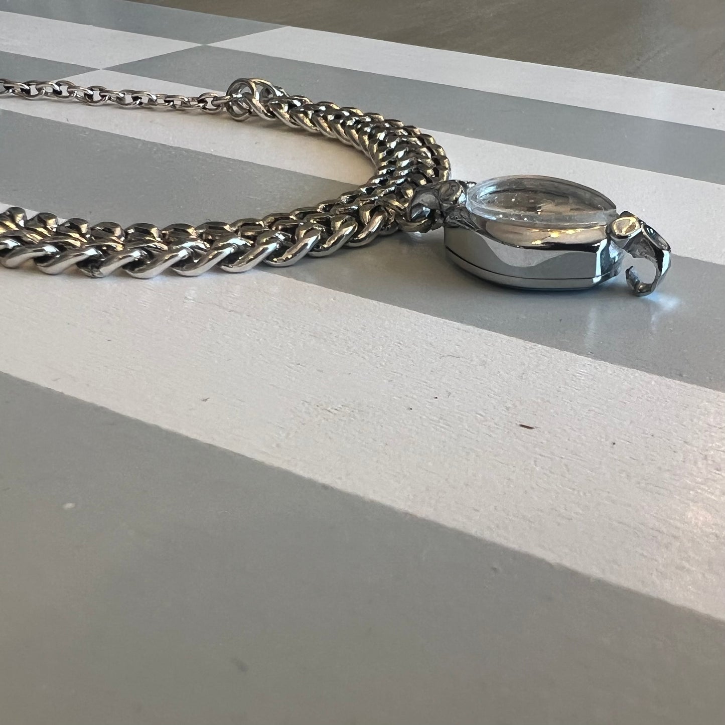 Timepiece /watch face part as pendant with a chunky mixed chain necklace partial side view.