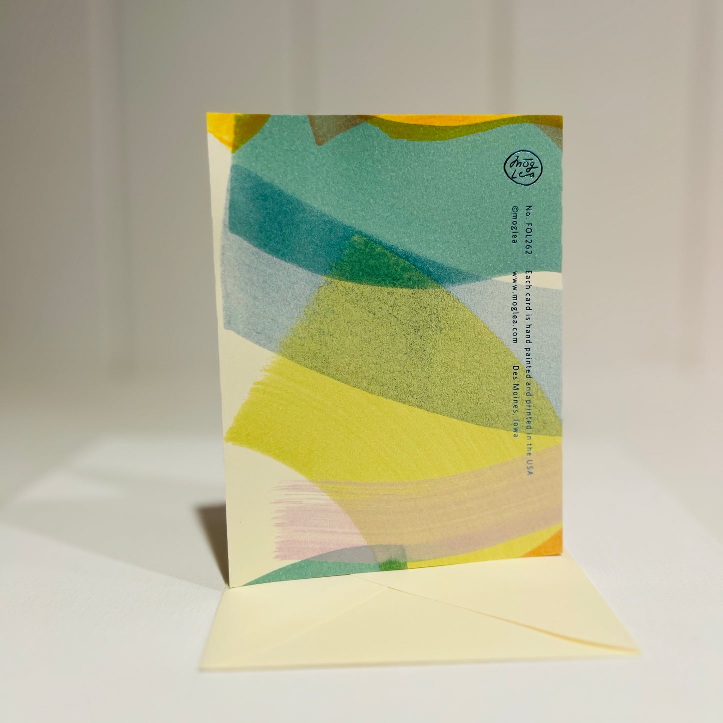 Back View Colorful card with abstract design and 'thank you' text on a light background with off white envelope. Lower case foil print.
Card standing upright on envelope.