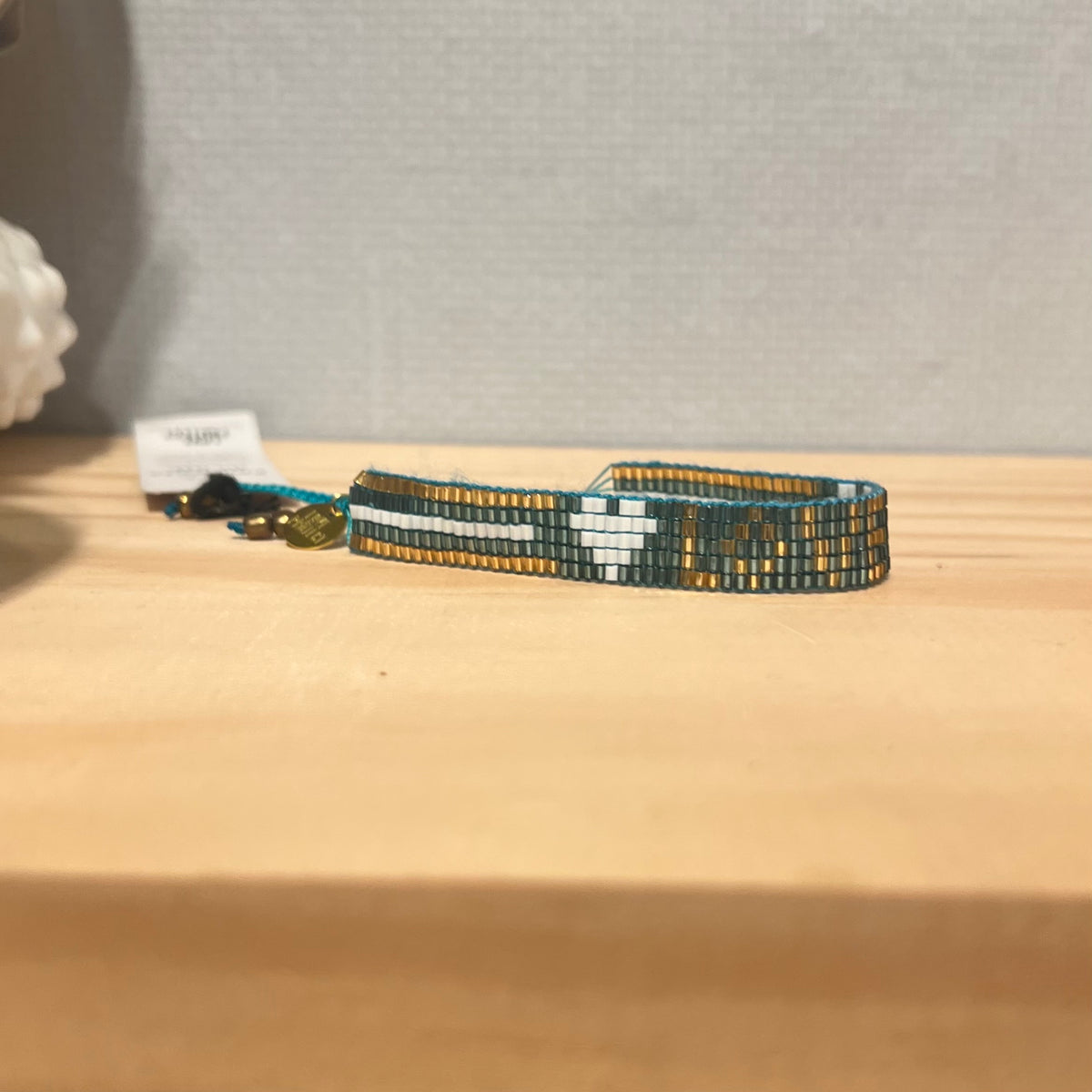 Side view of opal tone bead adjustable bracelet with white stripes and goldtone 'LOVE' beads, displayed on a wooden surface.