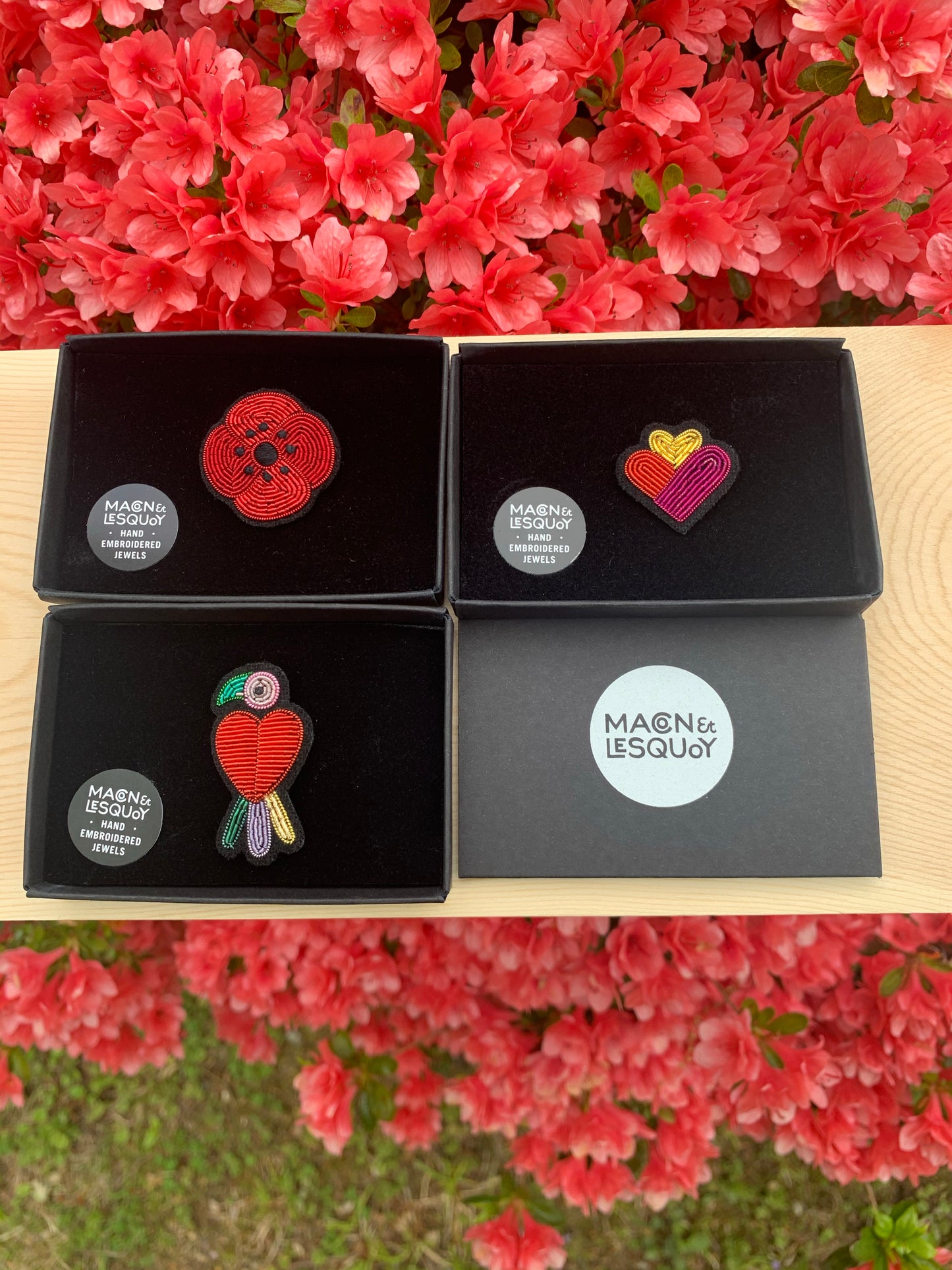 Designs of Macon and LesQuoy design brooches with velvet flock packaging and slide box tray with Logo sticker. Image for size comparison with other designs. Floral and greenery background.