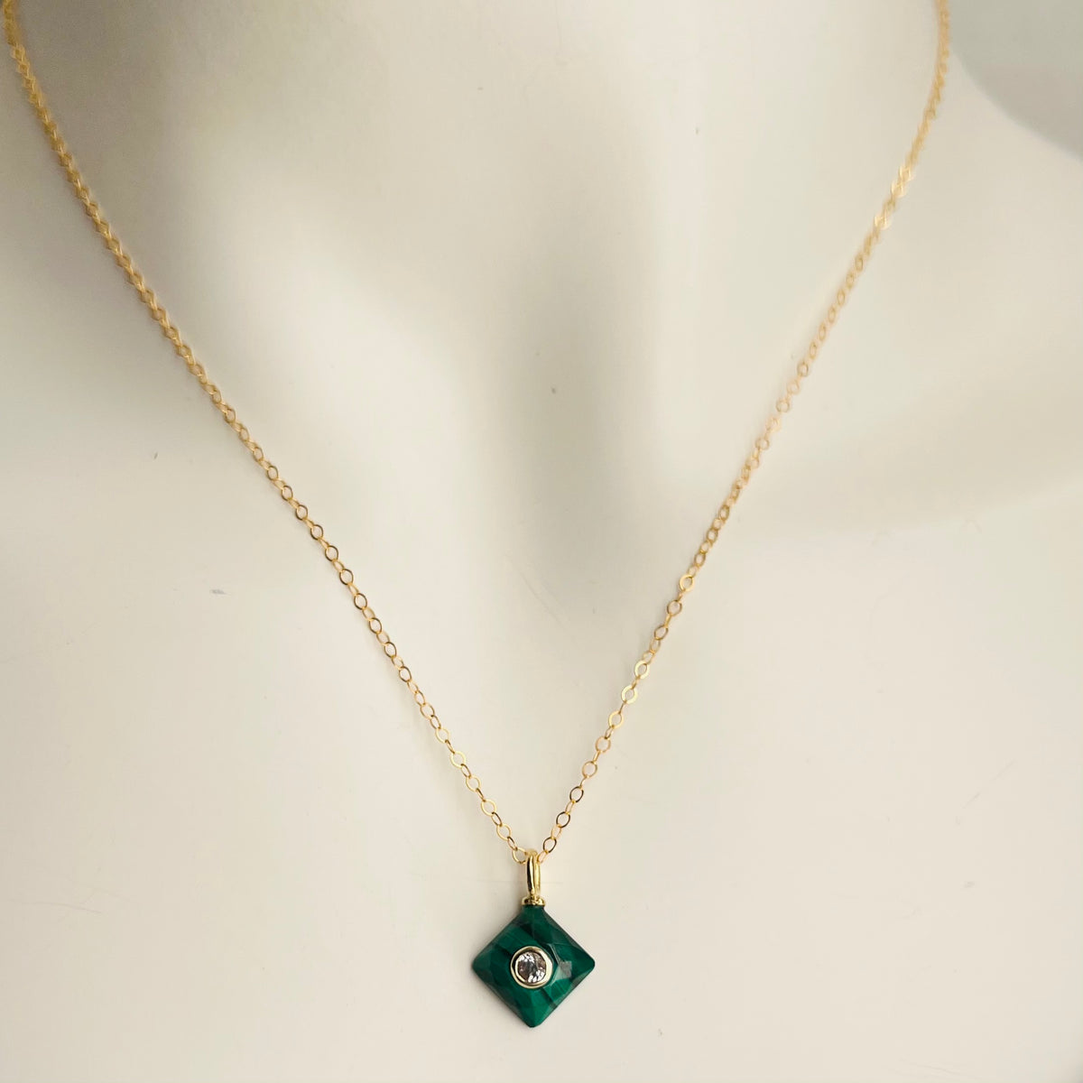 A gold filled chain necklace with a square malachite gemstone pendant in the center, displayed on a mannequin.