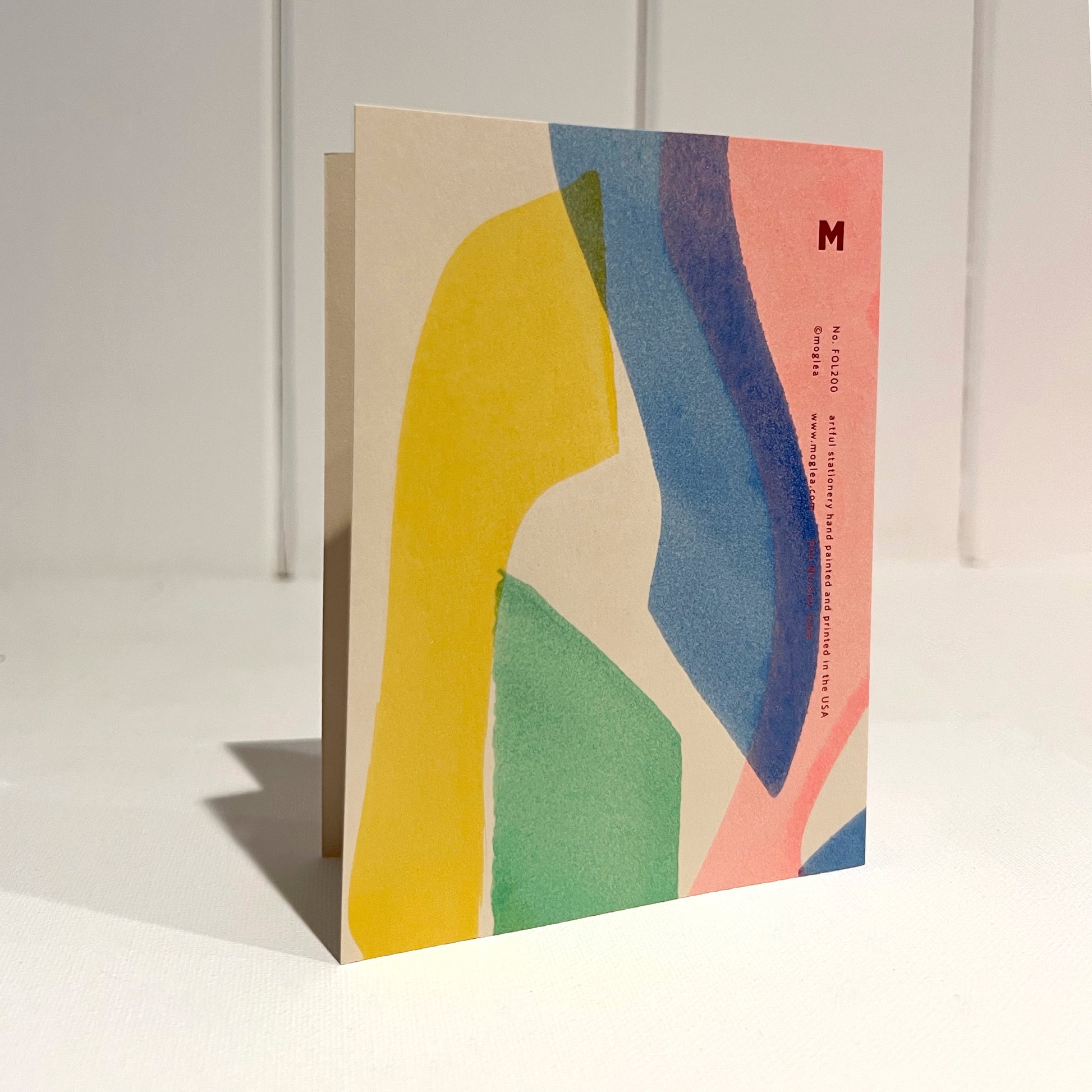 Hand painted multicolor folded card with script "happy birthday" color foil on offwhite background. Standing upright.