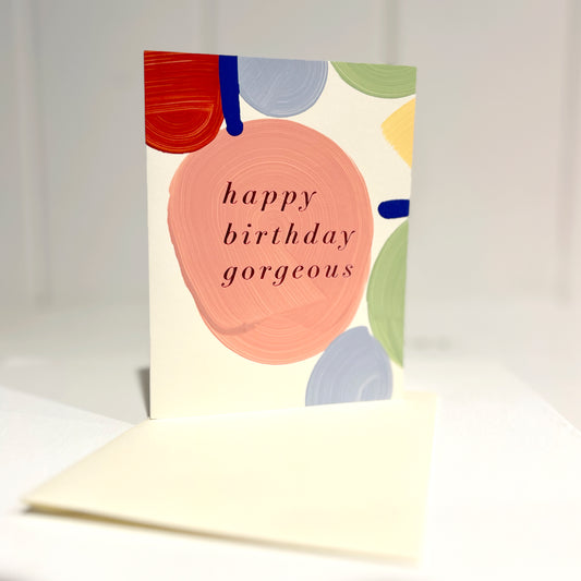Greeting card with colorful abstract design and 'happy birthday gorgeous' text on a off white background. Handpainted by Moglea
Front of Card upright on off white envelope.