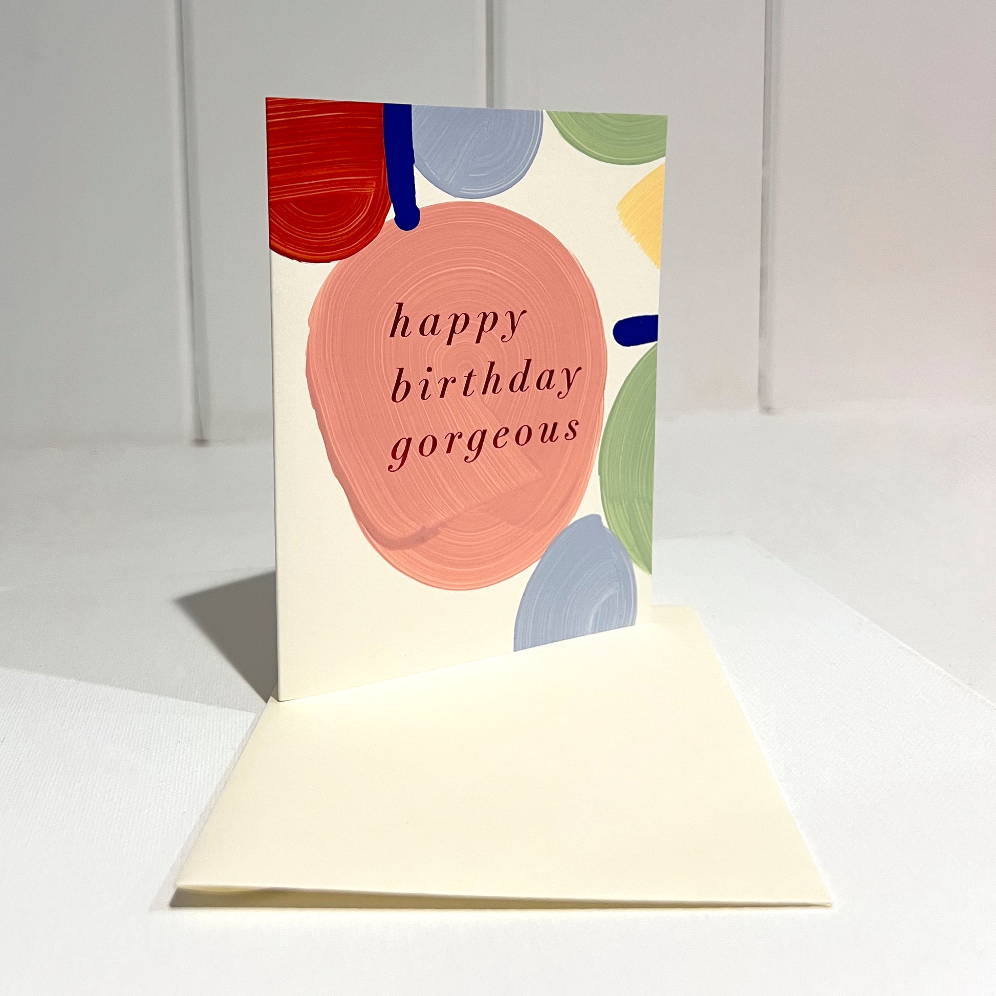 Greeting card with colorful abstract design and 'happy birthday gorgeous' text on a off white background.
Front of Card upright with envelope